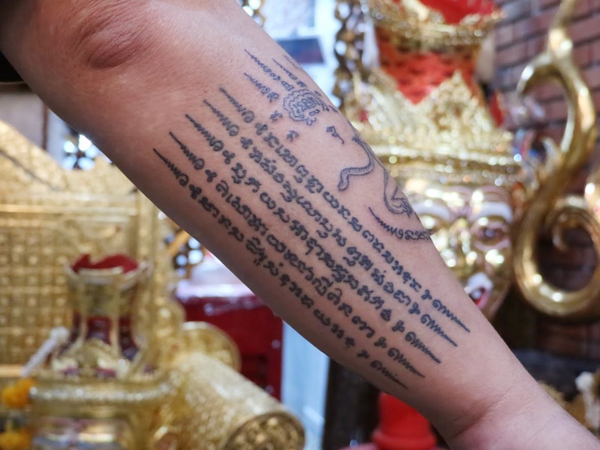 Bangkok, Thailand. 17th Jan, 2022. Sak Yant tattoo master Ajarn Neng sits  in his store in Bangkok's On Nut district, tattooing the back of a young  woman with a sharpened metal rod.